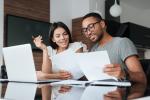 Two people sit at a table in front of a laptop and some papers.